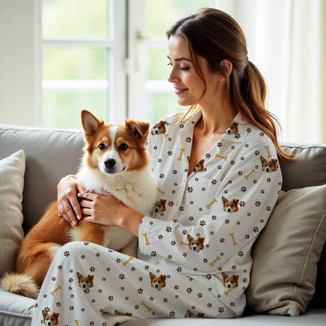 Kvinde i hvide personlige pyjamas med hundemotiv – Poteaftryk og benmønster, mens hun sidder med en brun og hvid hund på sofaen